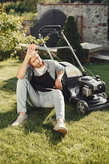 A well-maintained garden scene with a wooden bench positioned on a gravel pathway adjacent to lush, trimmed grass. The garden features a variety of plants and shrubs, including leafy green hedges and 